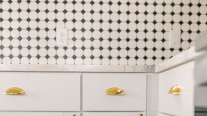 Una cocina con gabinetes blancos, detalles dorados y un salpicadero con estampado blanco y negro.