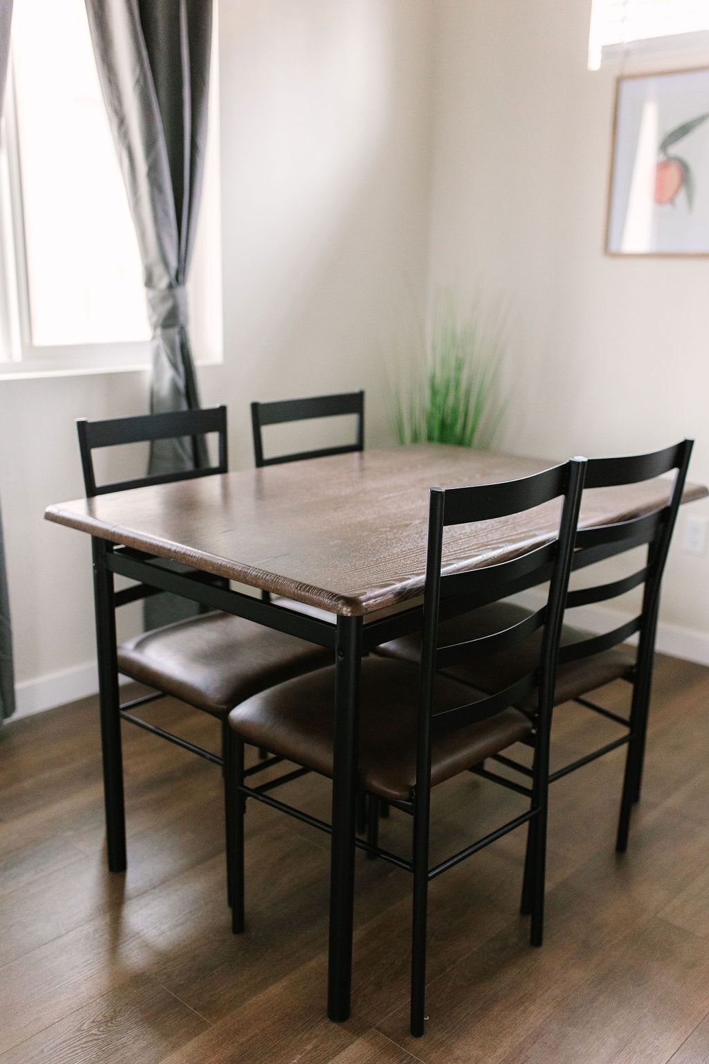 A dining table with four chairs, a window with curtains, and a framed picture on the wall.