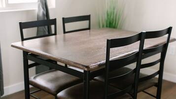 A dining table with four chairs, a window with curtains, and a framed picture on the wall.
