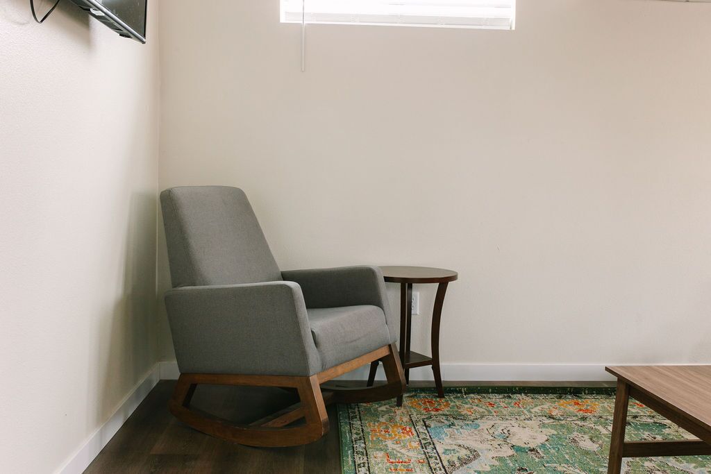 Een hoekzaal met een grijs gestoffeerde stoel, een klein rond tafeltje en een houten tafel.