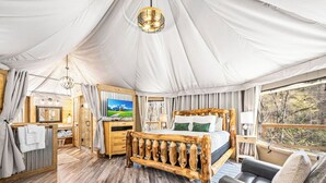 A tented room with a wooden bed, a TV, a desk, and a view of the outdoors. - Foxfire Tent (Bryson City)