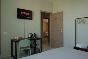 A hotel room with a bed, a desk with a chair, a television displaying 'NETFLIX', a door labeled '101', and a coat rack with hangers.