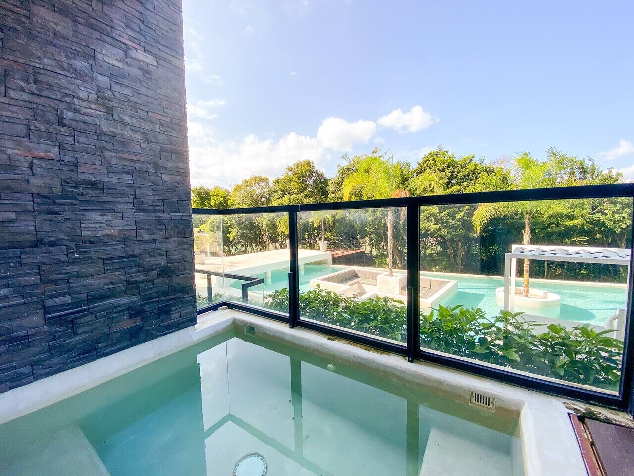 Une piscine intérieure moderne offrant une vue dégagée sur un espace piscine extérieur, le tout entouré d’une végétation luxuriante.