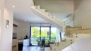 Un interno moderno con una scala, cucina, zona pranzo e ampie finestre.