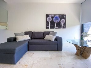 A modern living room with a grey sectional sofa, a glass coffee table, and a wall-mounted artwork of flowers.