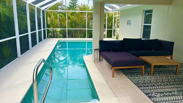 A pool area with a glass-enclosed structure, a sofa, and a patterned rug. - Perfect gateway!  (Bonita Springs)