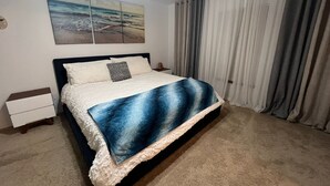 A bedroom with a bed, a nightstand, a wall-mounted painting, and a window with curtains. - Perfect gateway!  (Bonita Springs)