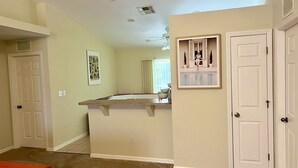 A hallway with a kitchen area, a ceiling fan, and a door with a decorative mirror. - Perfect gateway!  (Bonita Springs)