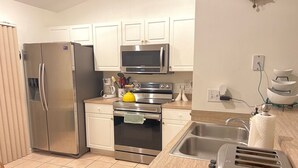 A modern kitchen with stainless steel appliances, white cabinetry, and a tiled floor. - Perfect gateway!  (Bonita Springs)