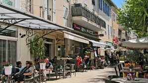 Een terras met tafels en stoelen, omringd door gebouwen met diverse winkels en restaurants.