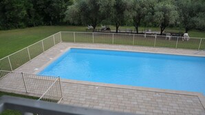 Une piscine rectangulaire avec une plage carrelée, entourée d’une clôture en métal blanc.