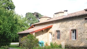 Un bâtiment en pierre avec un toit recouvert de tuiles rouges, un petit jardin et un chemin menant à l’entrée.