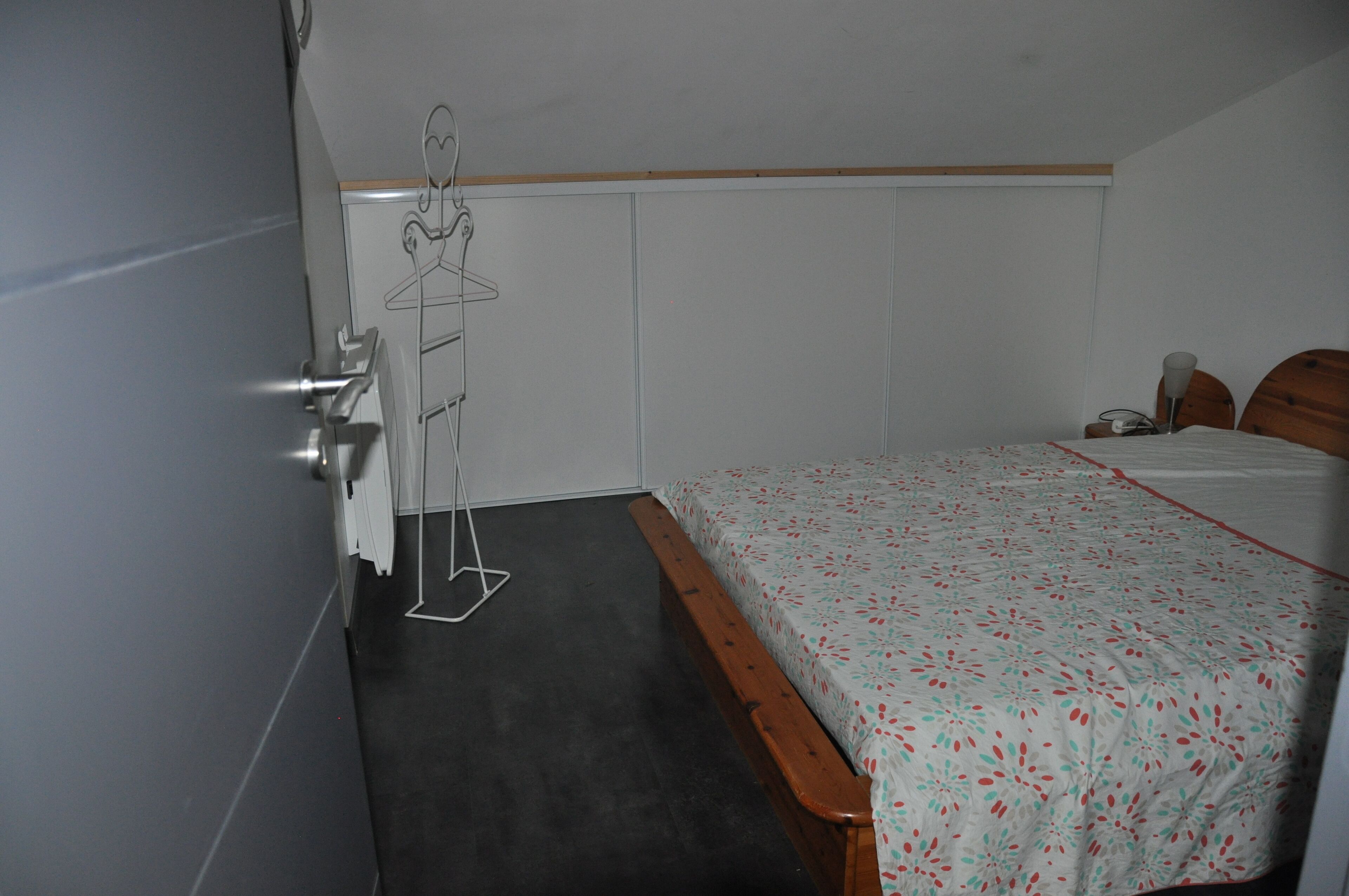 Quarto com cama, cabeceira de madeira, cabideiro e porta com uma toalha pendurada.