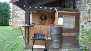 Un espace bar extérieur de style rustique, avec une structure en bois, un tonneau en métal et une petite table.