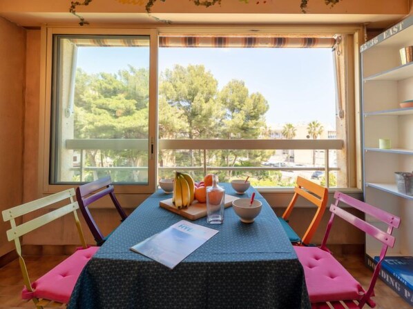 Una habitación con una mesa dispuesta para dos, una ventana con vistas a árboles, y una estantería a la derecha.