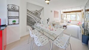A modern dining area with a glass table and white chairs, a ceiling fan, and a large wall mural of the Eiffel Tower. - Mare Nostrum by Interhome (Calpe/Calp)