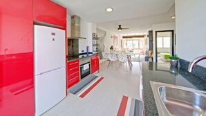 A modern kitchen with red cabinets, a white refrigerator, and a dining area with a striped rug. - Mare Nostrum by Interhome (Calpe/Calp)