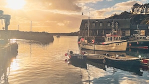 Un porto con imbarcazioni ormeggiate, un edificio con numerose finestre e un tramonto sullo sfondo.