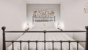Camera da letto con struttura del letto in metallo, testiera decorata con un'opera d'arte raffigurante un paesaggio urbano, due lampade da comodino e un termosifone.