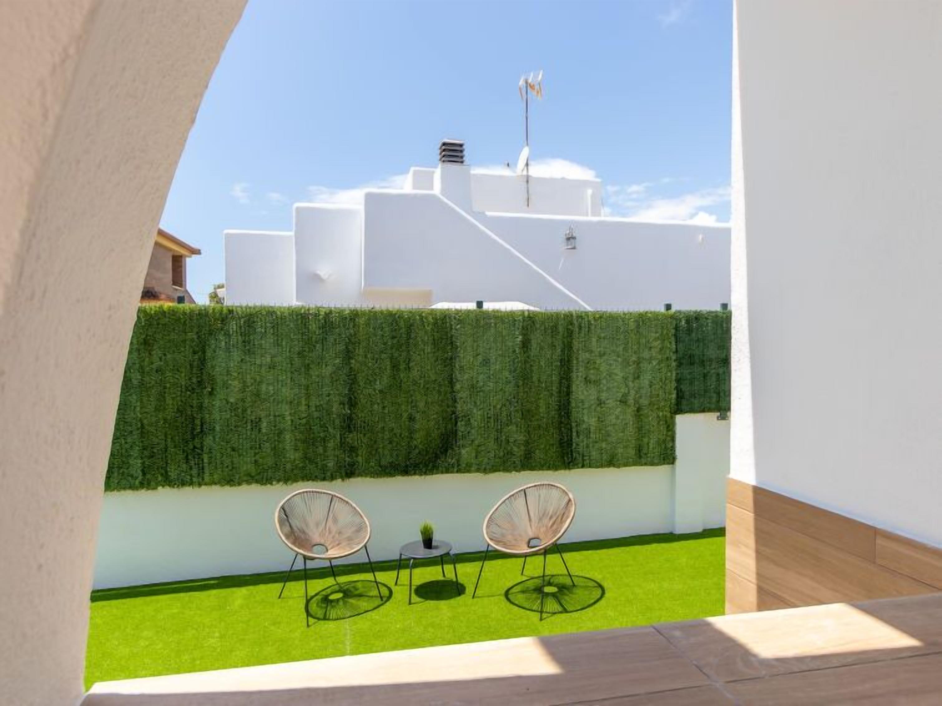 Une terrasse sur le toit avec deux chaises et une petite table, un arbuste taillé avec soin et, au fond, un bâtiment aux murs blancs et une cheminée.