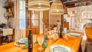 A wooden dining table with glassware and plates, two hanging wicker lamps, and a rustic stone wall. - Sa Caseta by Interhome (Ses Salines)
