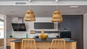 Una cocina moderna con una isla central, dos taburetes de mimbre, un frutero y un televisor de pantalla plana montado sobre la isla.
