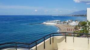 Vista costera con playa, un muelle y un edificio con balcones que dan al mar.