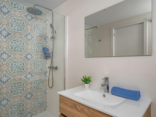 A bathroom with a shower, a sink, a mirror, and a potted plant.