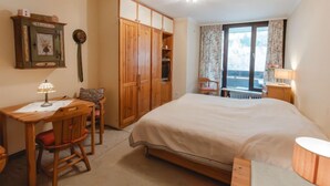 Une chambre à coucher comprenant un lit, une armoire en bois, un bureau, une chaise et une fenêtre avec des rideaux.