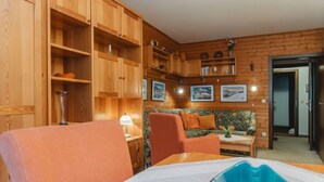 Une pièce chaleureuse avec des murs en bois, un canapé, un fauteuil et une table avec une lampe.