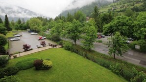 Un espace de stationnement où sont garées des voitures, entouré d’une végétation luxuriante et avec une chaîne de montagnes en arrière-plan.