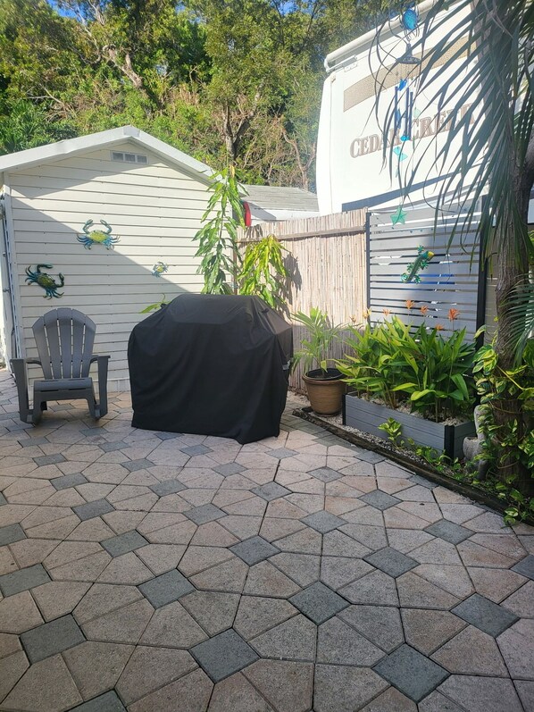 Een overdekt terras met een barbecue, een overdekte tafel en een stoel.