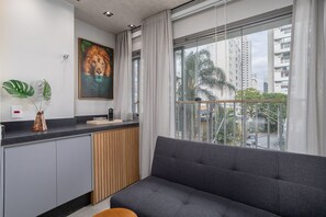 A modern living room with a grey sofa, a painting of a lion, and a view of tall buildings through large windows.