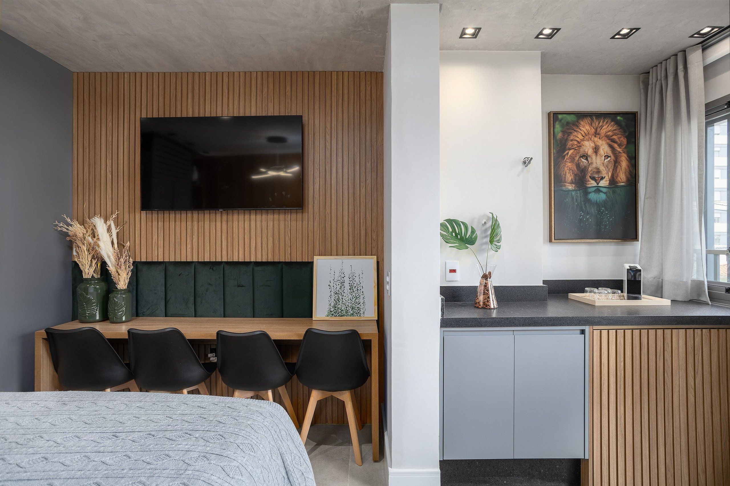 Quarto de hotel moderno com área de refeições em madeira, televisão de tela plana, obra de arte emoldurada e bancada de cozinha.