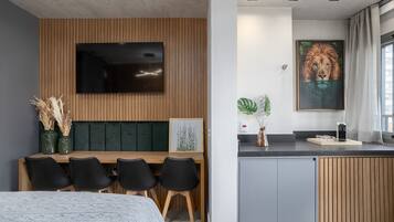 Quarto de hotel moderno com área de refeições em madeira, televisão de tela plana, obra de arte emoldurada e bancada de cozinha.