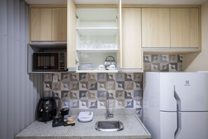 Una cocina compacta equipada con microondas, cafetera, lavabo y refrigerador.