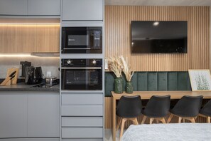 A compact kitchen with a microwave, oven, and coffee maker, a dining area with a table and chairs, and a flat-screen TV mounted on the wall.