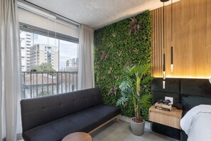 Una habitación moderna con sofá, mesita de noche con lámpara, planta en maceta y pared con plantas.