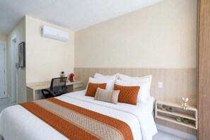Habitación de hotel con cama, escritorio, silla, cafetera, mesita de noche y aire acondicionado instalado en la pared.