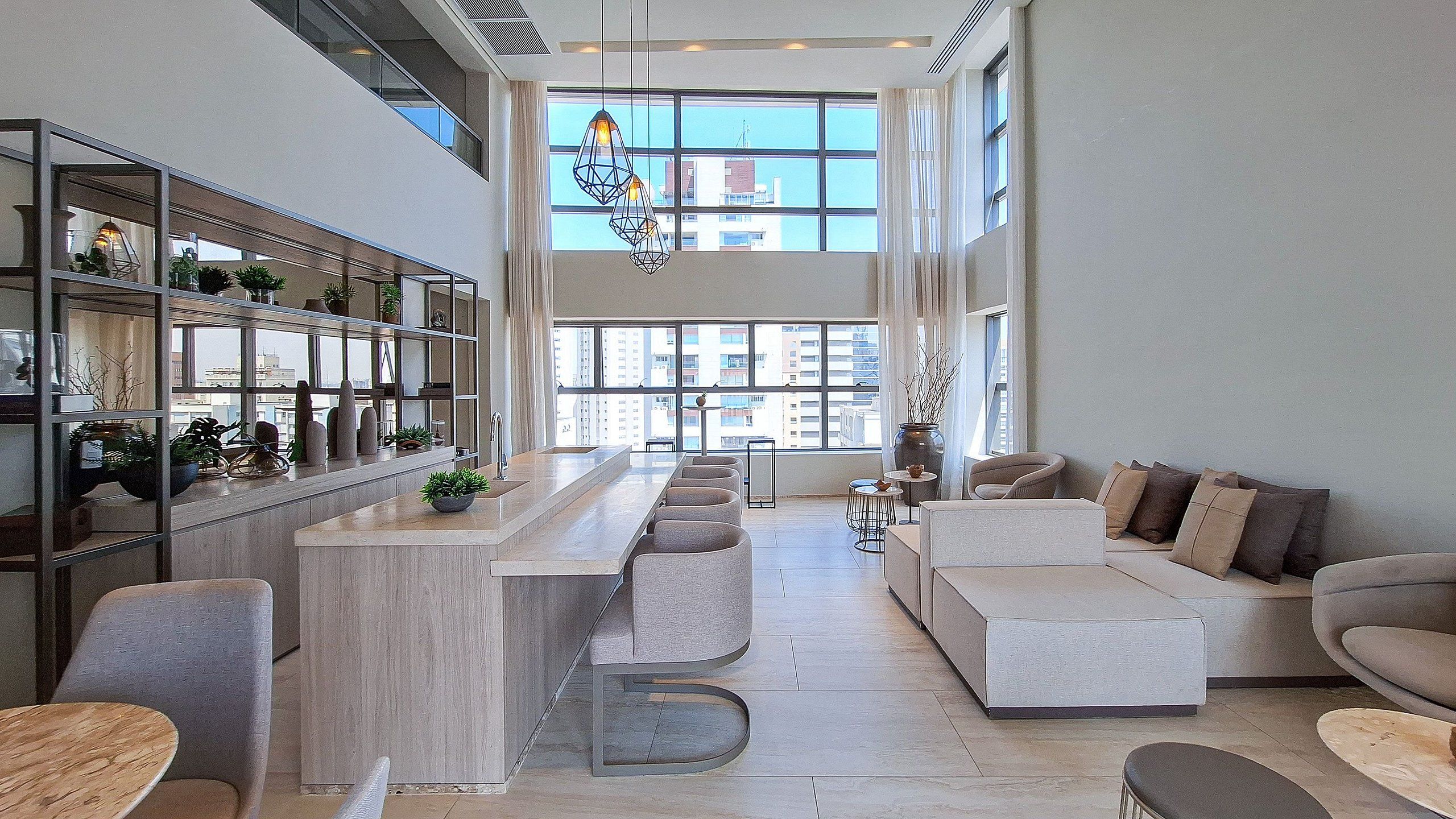 Un intérieur moderne avec un îlot de cuisine, un coin salon et de grandes fenêtres offrant une vue sur la ville.