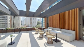 A rooftop terrace with outdoor seating, a wooden wall, and a view of surrounding buildings.
