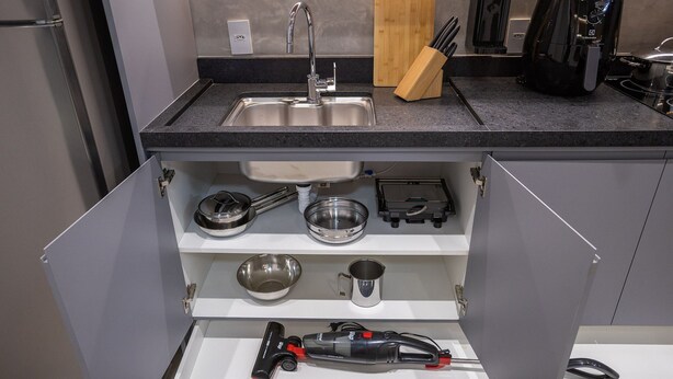 Una cocina con un lavamanos integrado, una cafetera y un aspirador guardado en un cajón.
