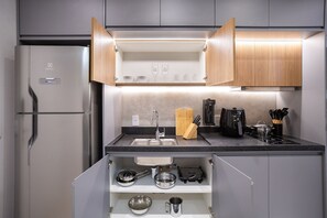 A compact kitchen with a built-in refrigerator, a sink, and a countertop with a coffee maker and utensils.