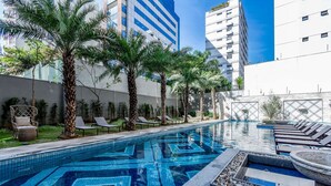 Una piscina con diseños de mosaicos, sillas de descanso, palmeras y edificios modernos al fondo.