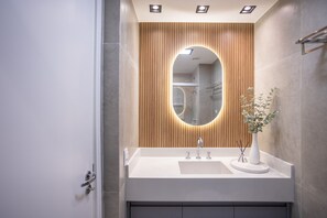 A modern bathroom with a wooden panel wall, a round mirror, and a white sink. - Zahle Jardins (São Paulo)