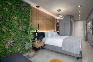 A modern bedroom with a green wall, a bed, a bedside table, and a potted plant.