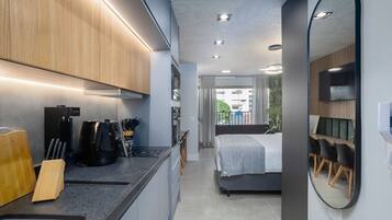Cozinha moderna com eletrodomésticos embutidos, sala de jantar com mesa e cadeiras, e quarto com cama e um espelho grande.