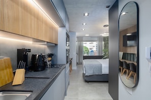 Una cocina moderna con electrodomésticos integrados, un comedor con mesa y sillas, y un dormitorio con cama y un espejo grande.