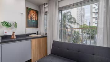 Uma sala de estar moderna com um sofá cinzento, um quadro de um leão e vista para edifícios altos através de grandes janelas.