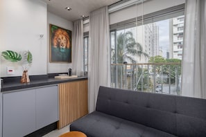 Una sala de estar moderna con un sofá gris, un cuadro de un león y vistas de edificios altos a través de amplias ventanas.